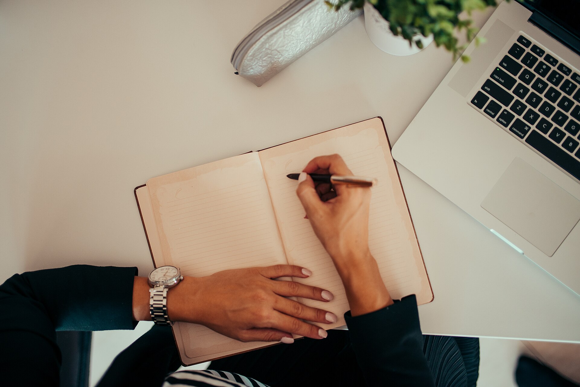 Vue de dessus d'un bureau : deux mains prennent des notes dans un carnet à côté d'un ordinateur portable — faire le point sur sa préparation au TCF