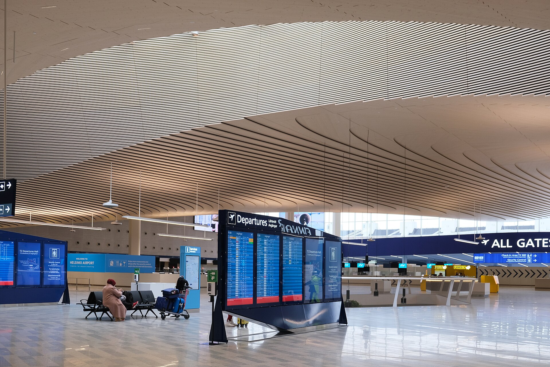 Hall de départs d'un aéroport moderne avec tableau des vols et voyageuse assise — partir travailler au Canada avec la Mobilité francophone